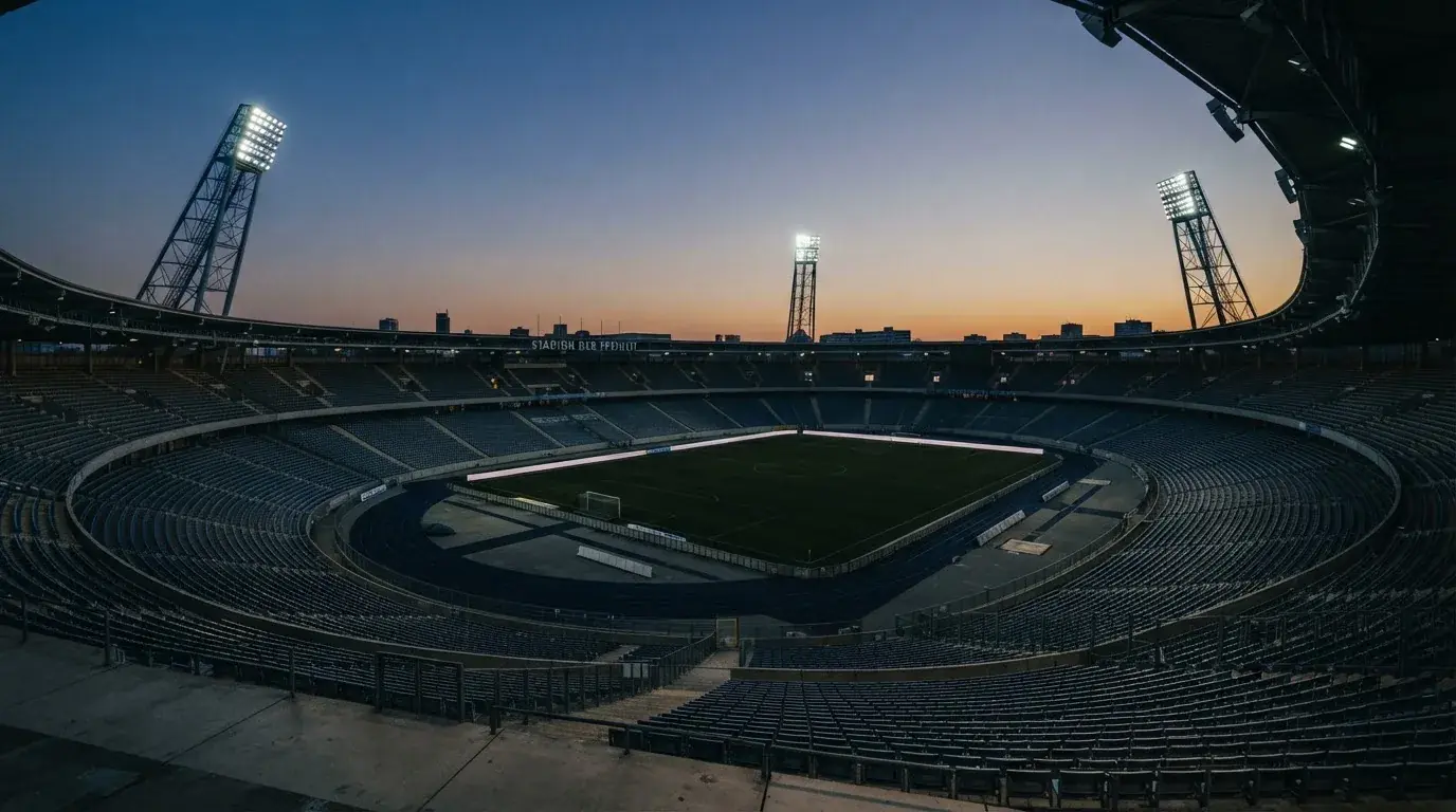 An empty football stadium with floodlight masts at dusk